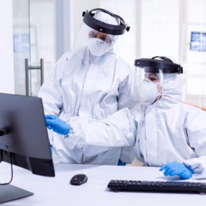 Doctor and nurse in ppe suit looking at monitor during global pandemic with covid-19. Medicine team wearing protection gear against coronavirus pandemic in dental reception as safety precaution.